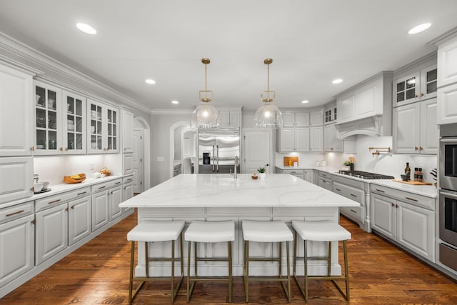 kitchen with light stone countertops, a center island with sink, tasteful backsplash, white cabinets, and appliances with stainless steel finishes