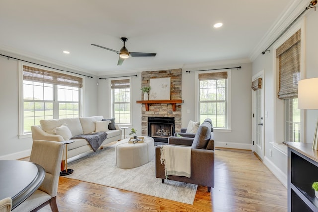 living room with ornamental molding, ceiling fan, light hardwood / wood-style floors, and a stone fireplace