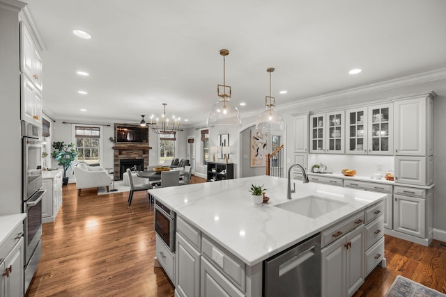 kitchen with sink, a fireplace, light stone counters, a kitchen island with sink, and appliances with stainless steel finishes