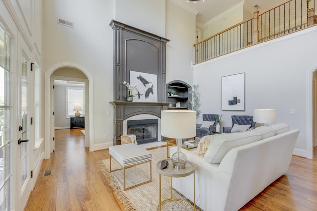 living room featuring light hardwood / wood-style floors, crown molding, and a towering ceiling