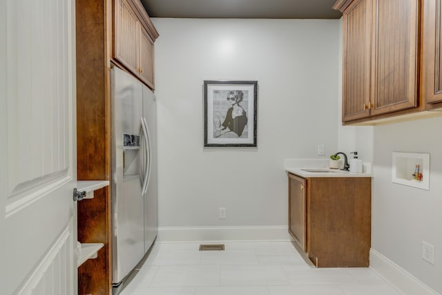 clothes washing area featuring sink, washer hookup, light tile patterned floors, and cabinets