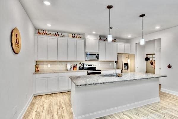 kitchen with white cabinets, appliances with stainless steel finishes, backsplash, and a kitchen island with sink