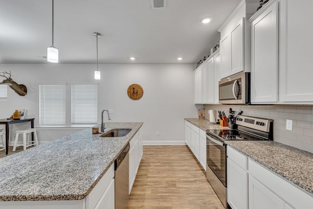 kitchen with decorative light fixtures, stainless steel appliances, a kitchen island with sink, white cabinetry, and sink