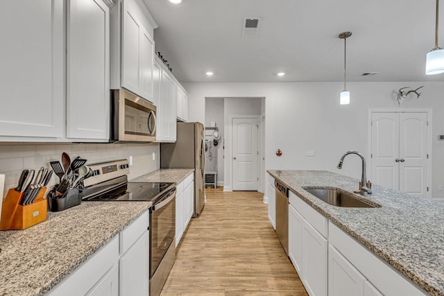 kitchen with light stone counters, decorative light fixtures, white cabinetry, appliances with stainless steel finishes, and sink