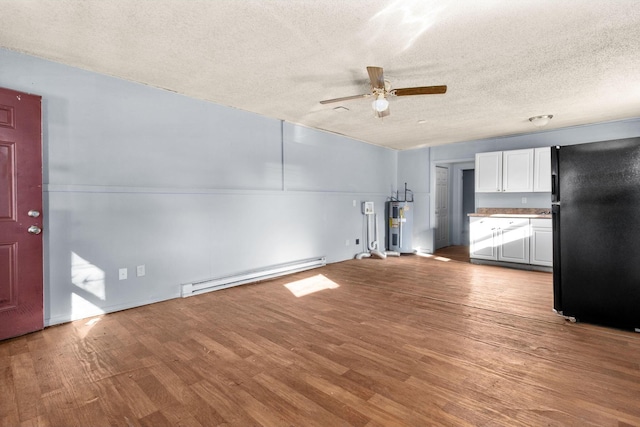 unfurnished living room with hardwood / wood-style floors, electric water heater, ceiling fan, a baseboard heating unit, and a textured ceiling