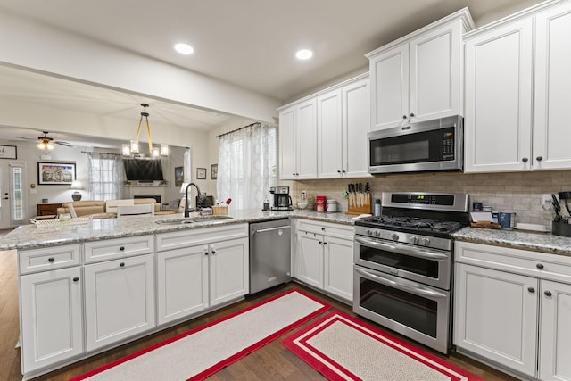 kitchen featuring kitchen peninsula, stainless steel appliances, ceiling fan with notable chandelier, white cabinets, and sink