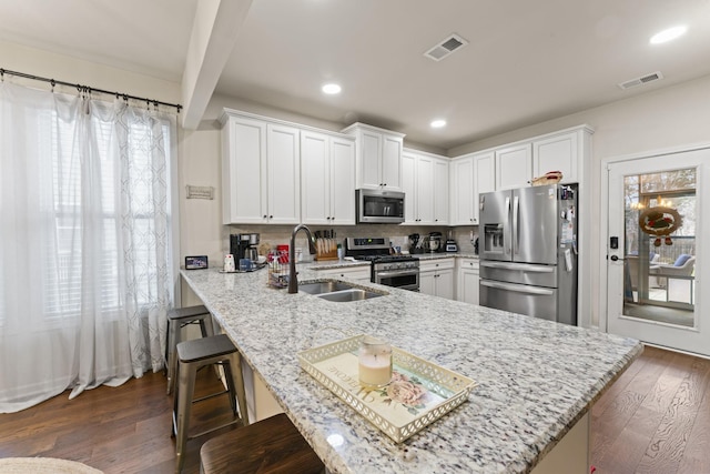 kitchen with stainless steel appliances, kitchen peninsula, a kitchen bar, sink, and white cabinetry