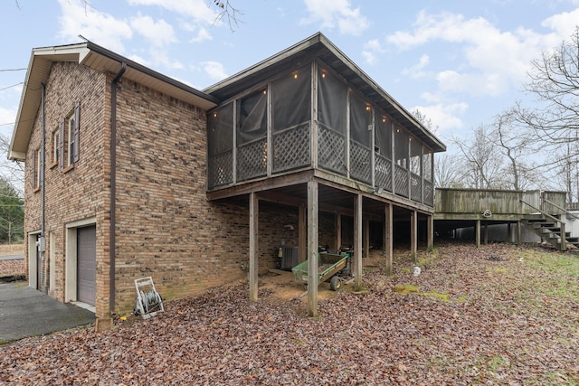 rear view of property featuring a sunroom, a deck, and a garage