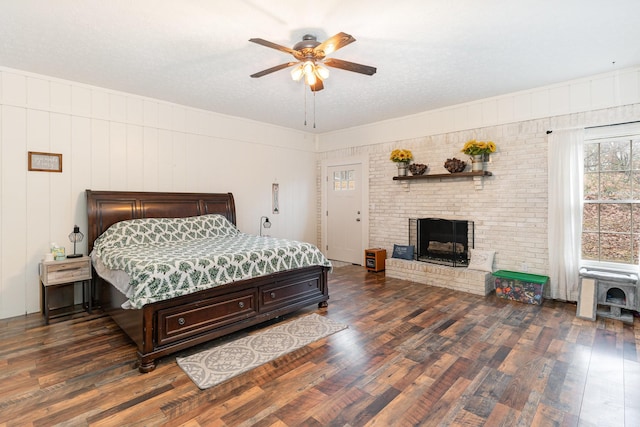 bedroom with ceiling fan, a textured ceiling, dark hardwood / wood-style floors, and a brick fireplace