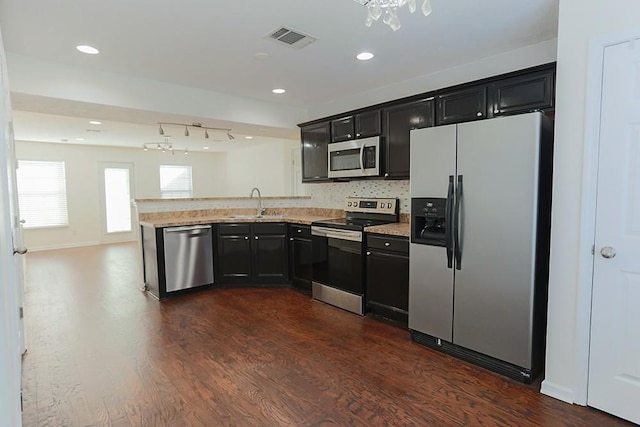 kitchen with stainless steel appliances, sink, light stone counters, decorative backsplash, and dark hardwood / wood-style floors