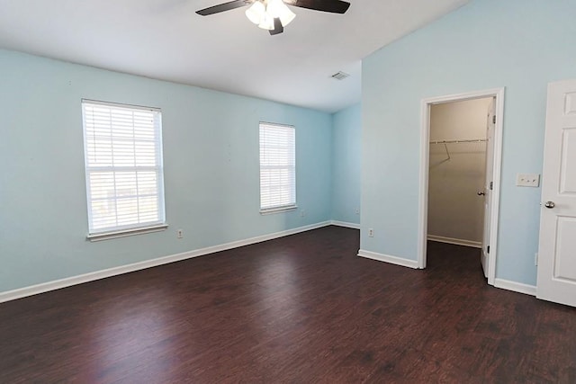 unfurnished bedroom featuring vaulted ceiling, ceiling fan, a closet, a walk in closet, and dark hardwood / wood-style flooring