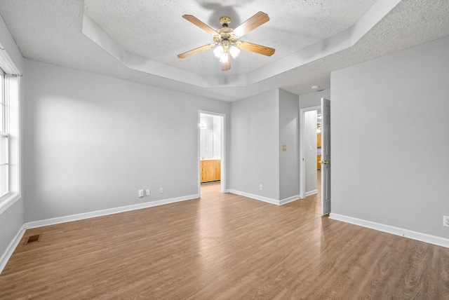 empty room featuring a textured ceiling, light hardwood / wood-style flooring, a raised ceiling, plenty of natural light, and ceiling fan