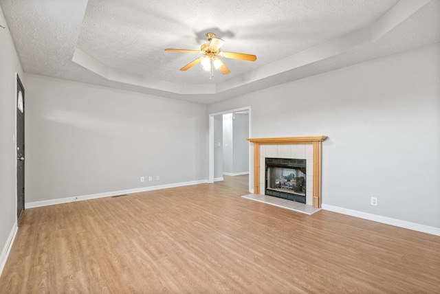 unfurnished living room with a textured ceiling, a fireplace, ceiling fan, light hardwood / wood-style flooring, and a tray ceiling