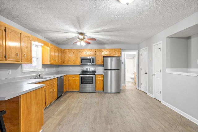 kitchen with appliances with stainless steel finishes, light wood-type flooring, kitchen peninsula, ceiling fan, and sink