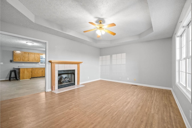 unfurnished living room featuring a textured ceiling, a fireplace, a raised ceiling, ceiling fan, and light hardwood / wood-style floors