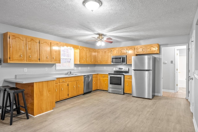 kitchen with stainless steel appliances, ceiling fan, light hardwood / wood-style flooring, kitchen peninsula, and a breakfast bar area