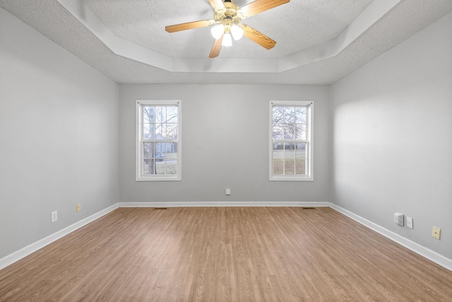 empty room featuring a textured ceiling, ceiling fan, a tray ceiling, and light hardwood / wood-style floors