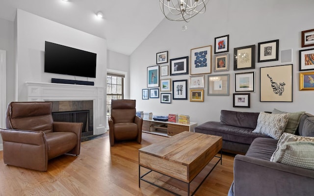 living room featuring high vaulted ceiling, a fireplace, a chandelier, and light hardwood / wood-style floors