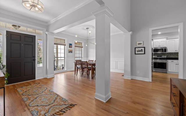 entrance foyer with decorative columns, a notable chandelier, light hardwood / wood-style flooring, and ornamental molding