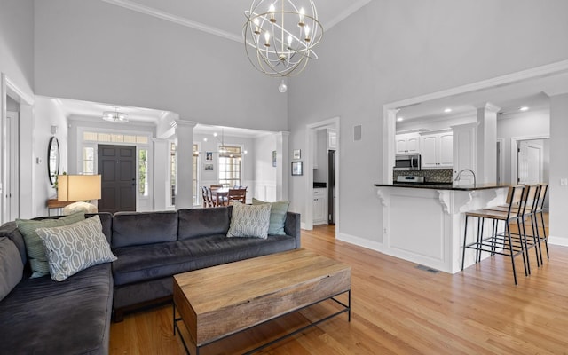 living room with a high ceiling, light hardwood / wood-style floors, crown molding, and a chandelier