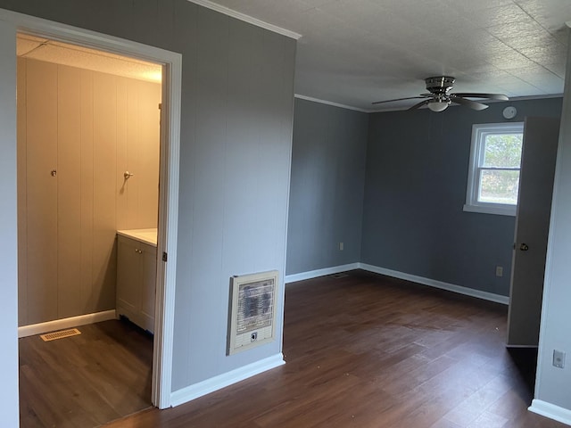 spare room featuring dark wood-type flooring, ceiling fan, ornamental molding, and heating unit