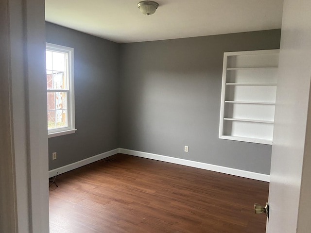 spare room featuring built in shelves and dark wood-type flooring