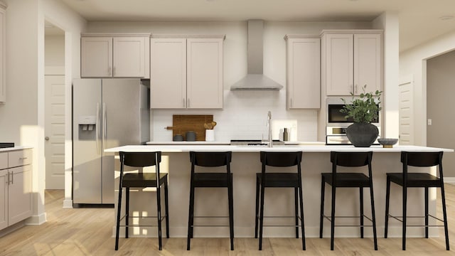 kitchen featuring light hardwood / wood-style floors, stainless steel fridge with ice dispenser, an island with sink, a kitchen bar, and wall chimney range hood