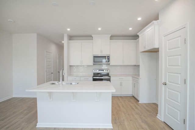 kitchen featuring stainless steel appliances, an island with sink, sink, and white cabinetry