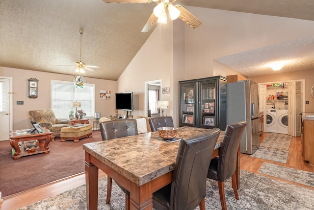 dining area with a textured ceiling, ceiling fan, light hardwood / wood-style floors, separate washer and dryer, and high vaulted ceiling