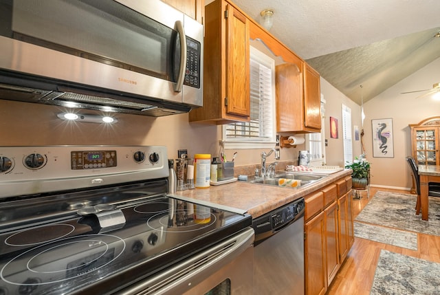 kitchen featuring sink, a textured ceiling, lofted ceiling, light hardwood / wood-style floors, and appliances with stainless steel finishes