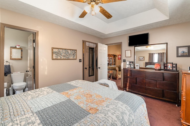 bedroom with ensuite bathroom, ceiling fan, a tray ceiling, and dark colored carpet