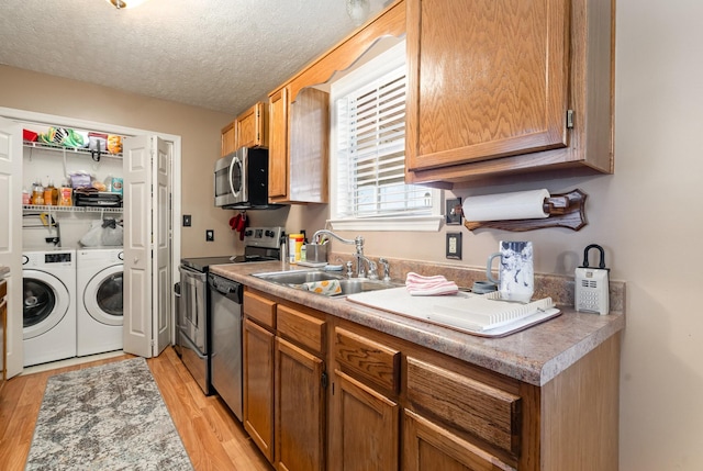 kitchen with appliances with stainless steel finishes, light hardwood / wood-style floors, a textured ceiling, sink, and washing machine and clothes dryer