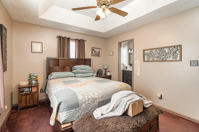 carpeted bedroom with ceiling fan, ensuite bath, and a raised ceiling