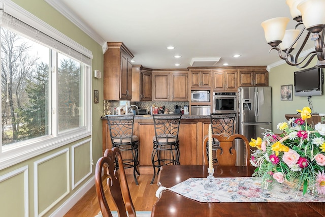 kitchen featuring stainless steel appliances, an inviting chandelier, light hardwood / wood-style floors, a breakfast bar, and crown molding