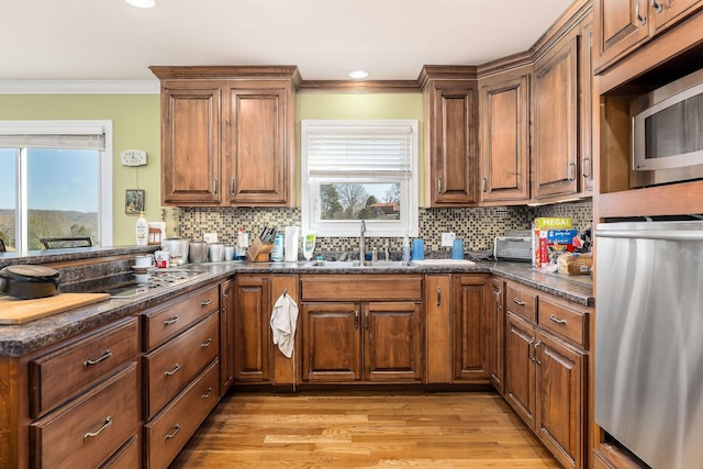 kitchen with dark stone countertops, light wood-type flooring, crown molding, stainless steel microwave, and sink