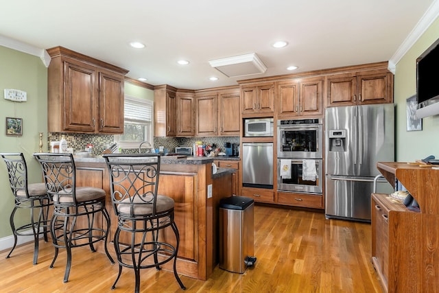 kitchen with stainless steel appliances, light wood-type flooring, crown molding, a kitchen bar, and tasteful backsplash