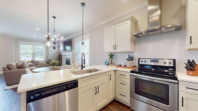 kitchen with stainless steel appliances, sink, wall chimney exhaust hood, kitchen peninsula, and pendant lighting