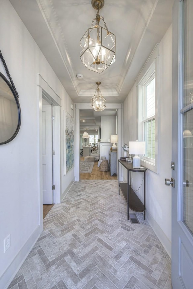 hall featuring crown molding, an inviting chandelier, and a raised ceiling