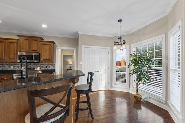 kitchen featuring stainless steel appliances, a breakfast bar area, decorative backsplash, dark stone counters, and hanging light fixtures