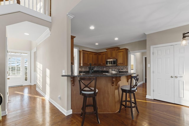 kitchen with kitchen peninsula, stainless steel appliances, a kitchen breakfast bar, and dark hardwood / wood-style floors