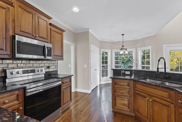 kitchen with stainless steel appliances, hanging light fixtures, dark stone counters, dark hardwood / wood-style flooring, and sink