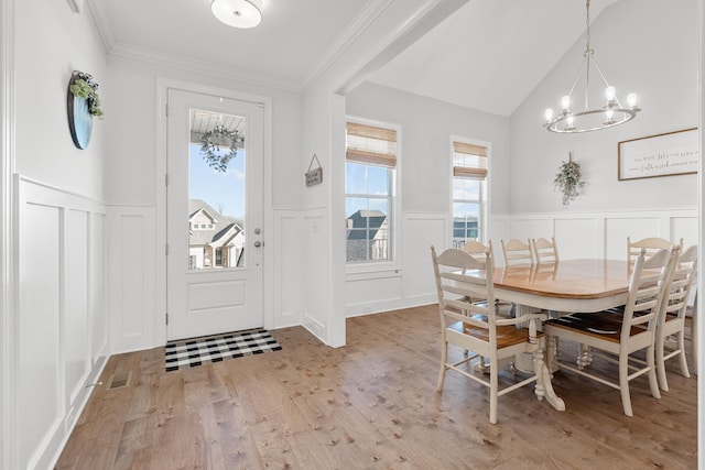 dining space with crown molding, light hardwood / wood-style flooring, lofted ceiling, and a chandelier