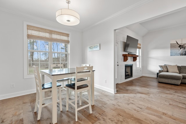 dining area featuring a large fireplace, ornamental molding, light hardwood / wood-style flooring, and plenty of natural light