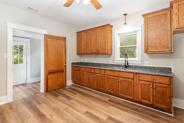 kitchen with light wood-type flooring, dark stone countertops, pendant lighting, and sink