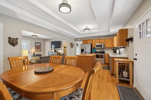 dining space featuring sink, light wood-type flooring, and a raised ceiling