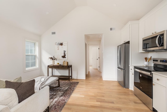 kitchen with stainless steel appliances, high vaulted ceiling, white cabinetry, and light wood-type flooring