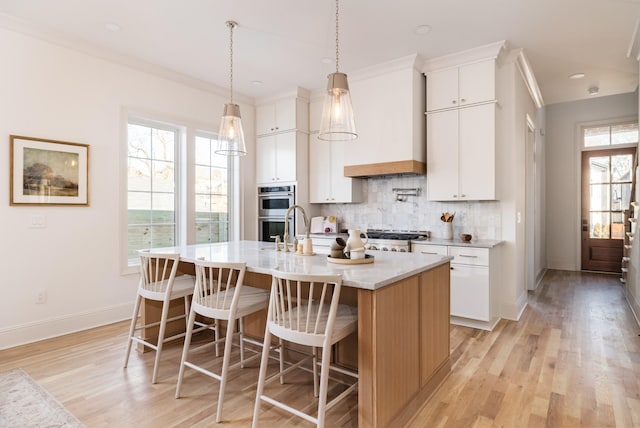 kitchen with white cabinets, light wood-type flooring, a kitchen island with sink, and decorative backsplash