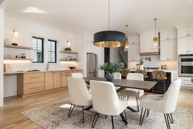 dining area featuring sink, light wood-type flooring, and crown molding