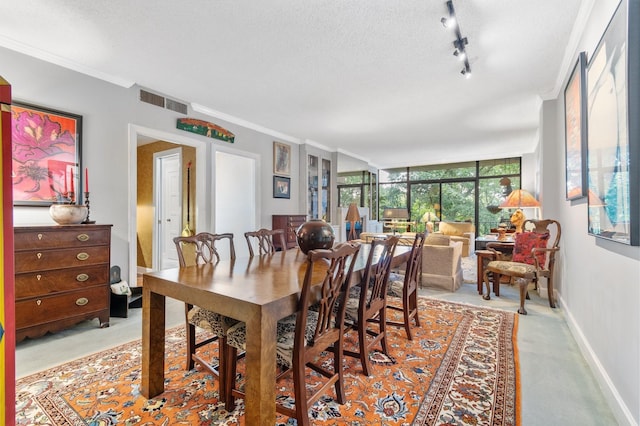 dining area with track lighting, a textured ceiling, a wall of windows, and crown molding