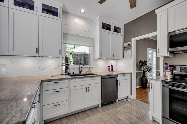 kitchen with stainless steel appliances, ceiling fan, light stone counters, sink, and white cabinetry